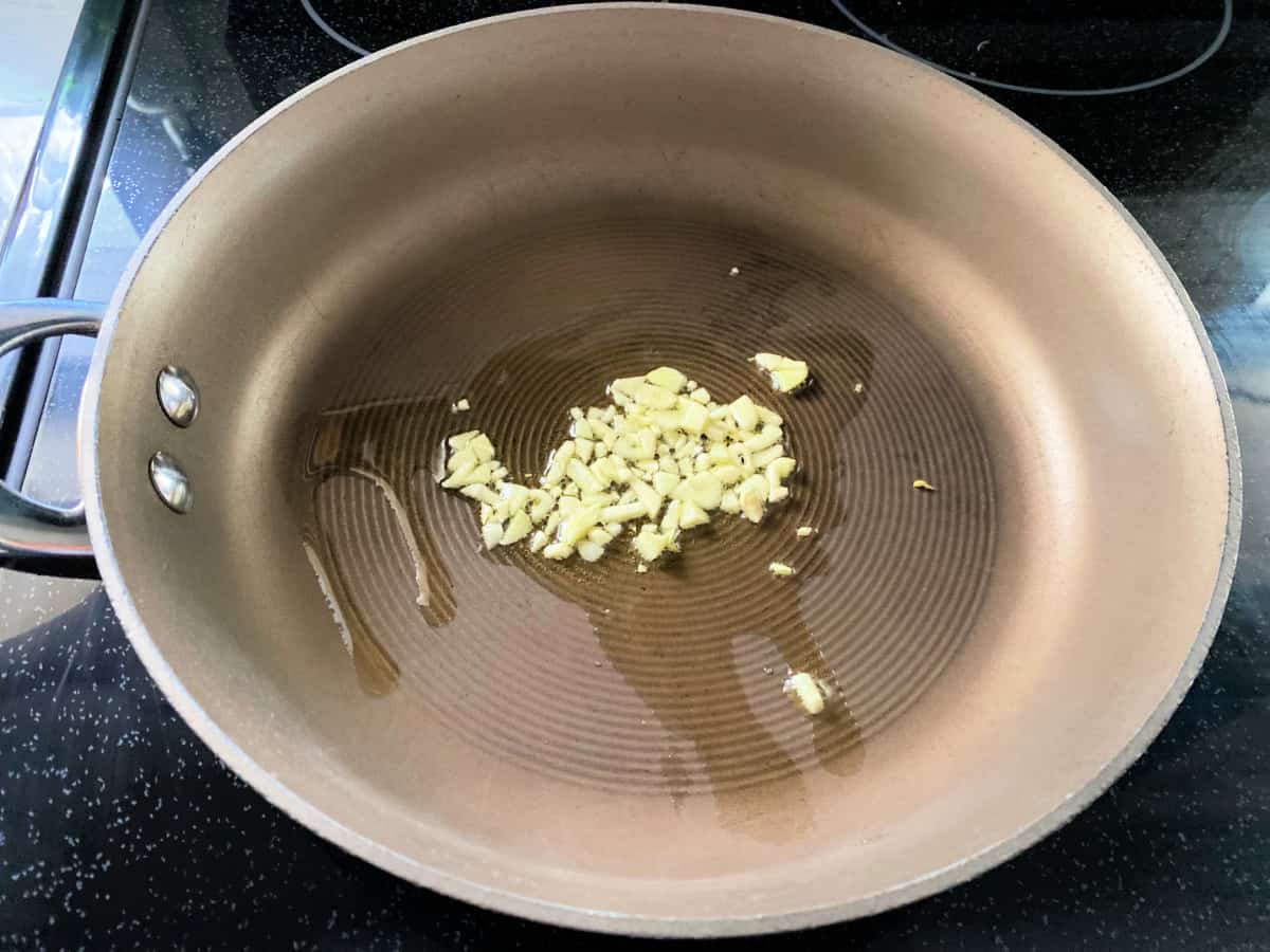 Brown frying pan with chopped garlic and oil in pan.