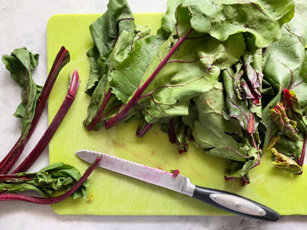 Green cutting board with chopped greens and a knife.