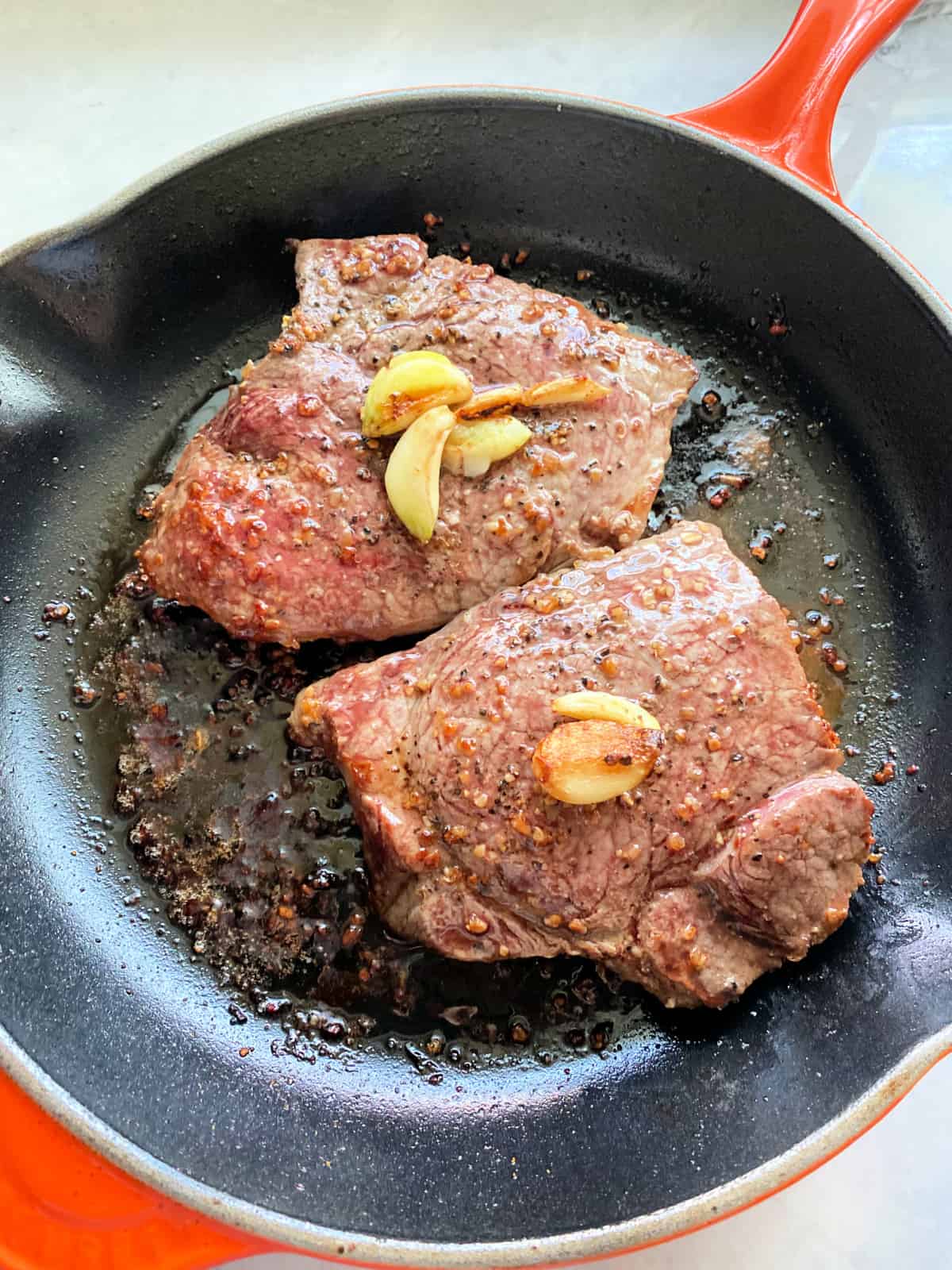 Two pieces of steak seared on a skillet with garlic on top.