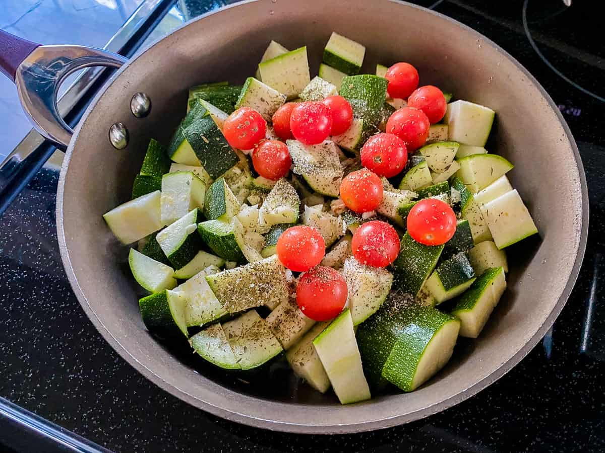 seasoned diced zucchini and grape tomatoes cooking in a pan.