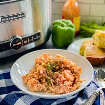 White bowl filled with rice, shrimp, and sausage with spoon next to it.