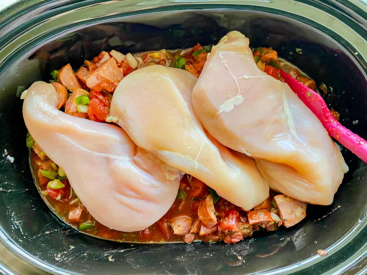 Oval black dish filled with tomato mixture and 3 chicken breast.