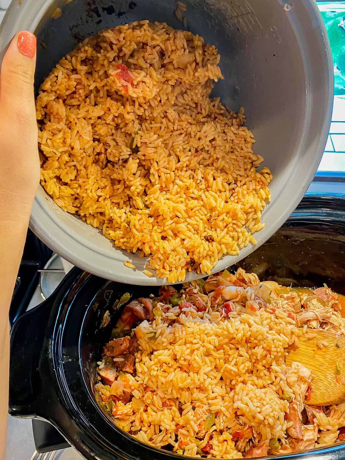 Female hand pouring cooked rice from a silver pot into a black oval pot.