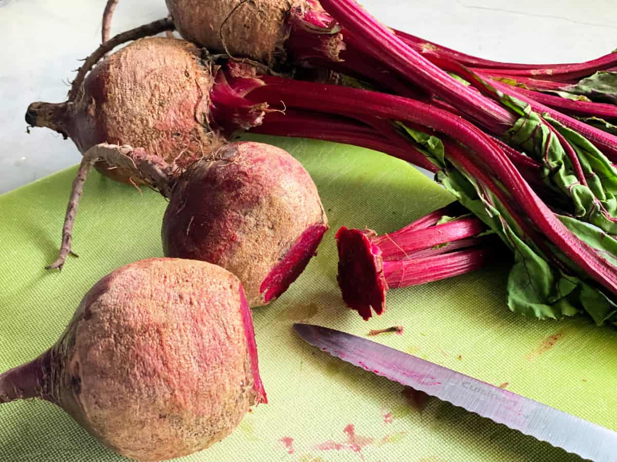 Raw beets with tops cut off sitting on a cutting board with a knife.