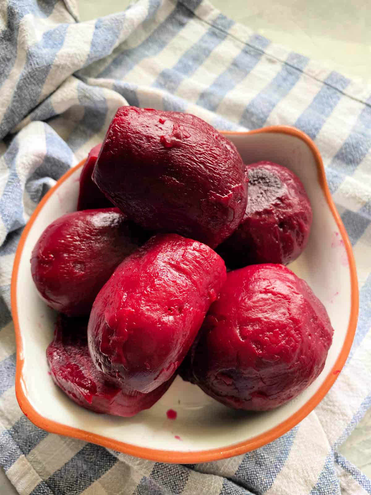 White bowl filled with cooked beets on a blue and white checkered cloth.