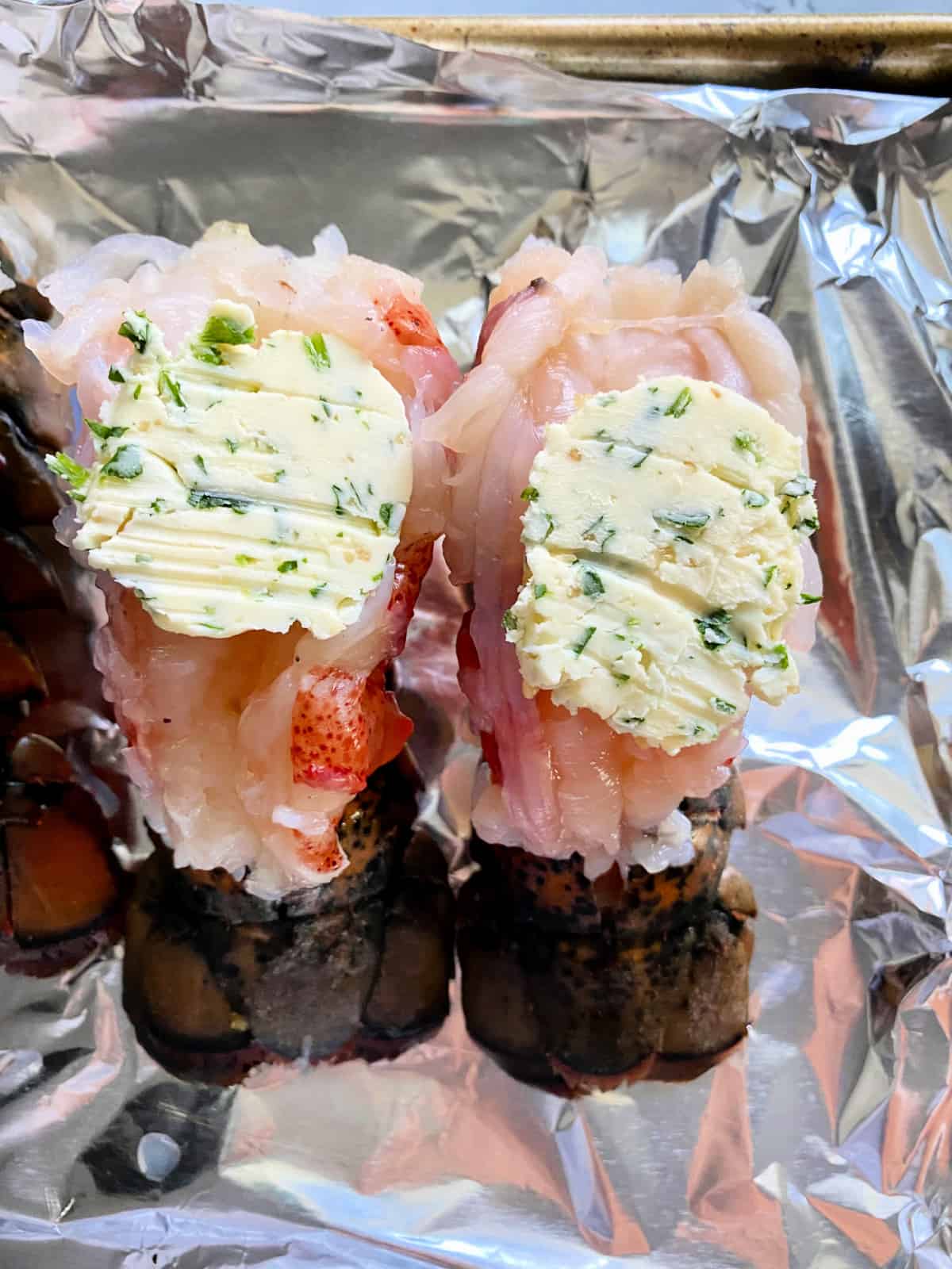 Two lobster tails with herb compound butter on top.