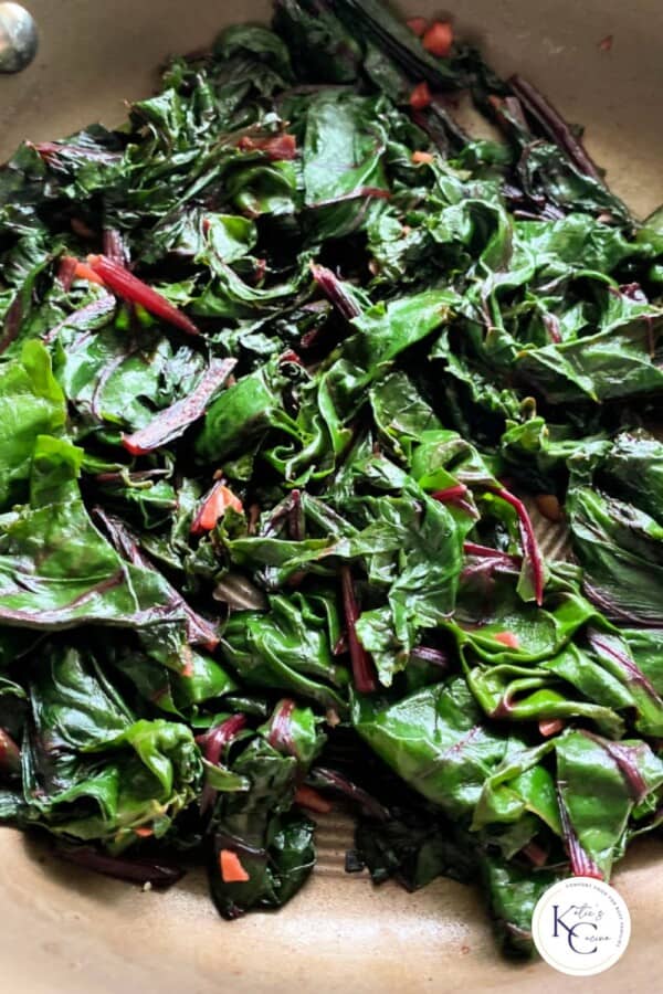 Sauteed greens in brown skillet with logo on right corner.