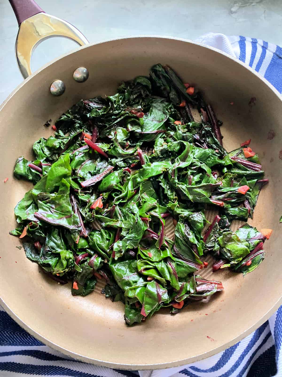 Sauteed greens with chopped garlic in a brown saute pan.