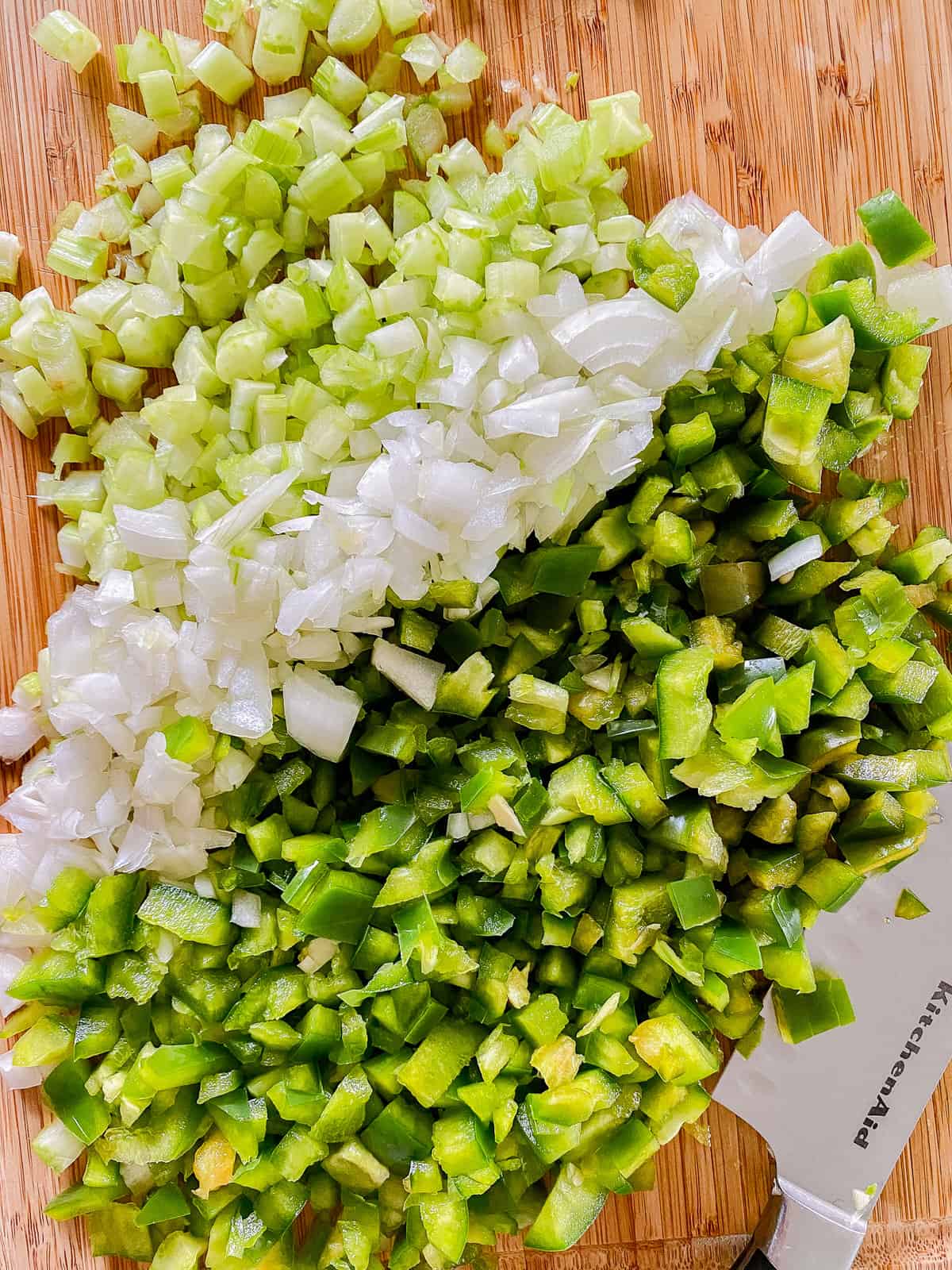 Diced celery, onion, and bell pepper on a cutting board with a knife next to it.