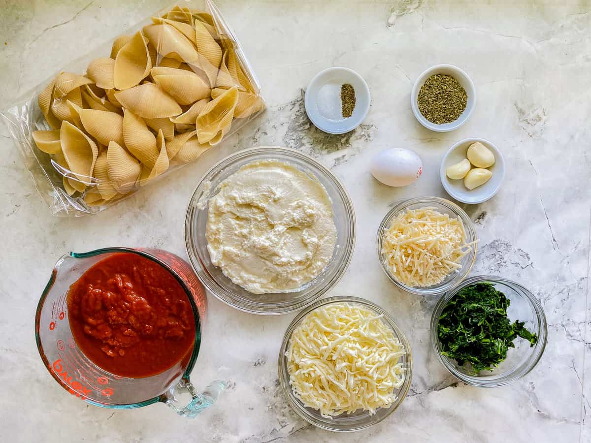 Ingredients for the Spinach Stuffed Shells are present upon a white marble countertop.