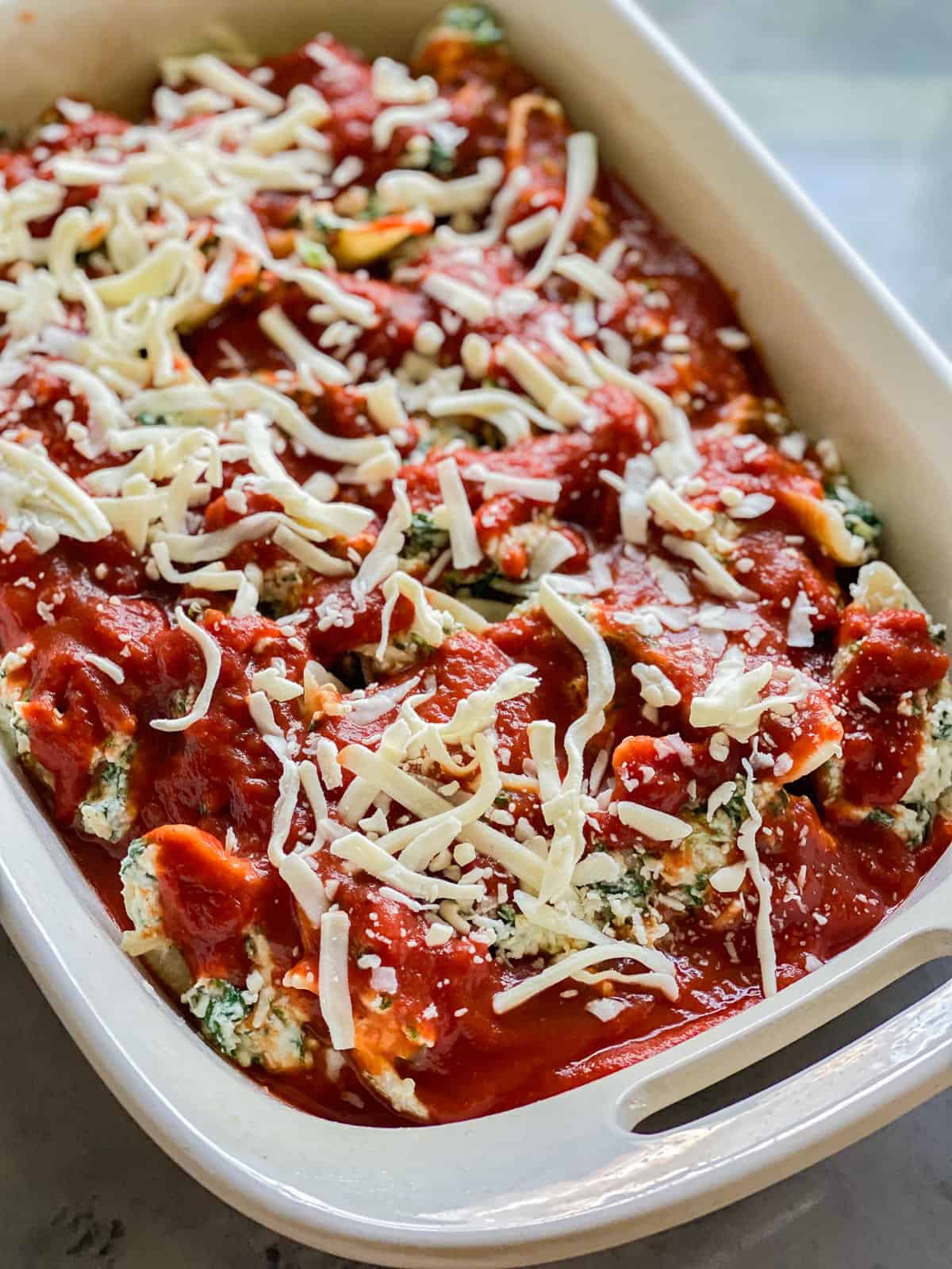 Stuffed Spinach Shells topped with mozzarella cheese in a white baking dish.