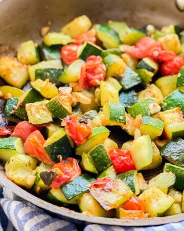 Close up shot of sautéed zucchini and tomatoes resting in a pan.