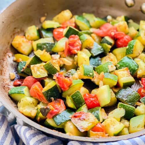 Close up shot of sautéed zucchini and tomatoes resting in a pan.