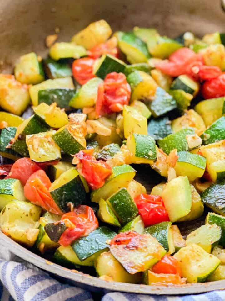 Close up shot of sautéed zucchini and tomatoes resting in a pan.