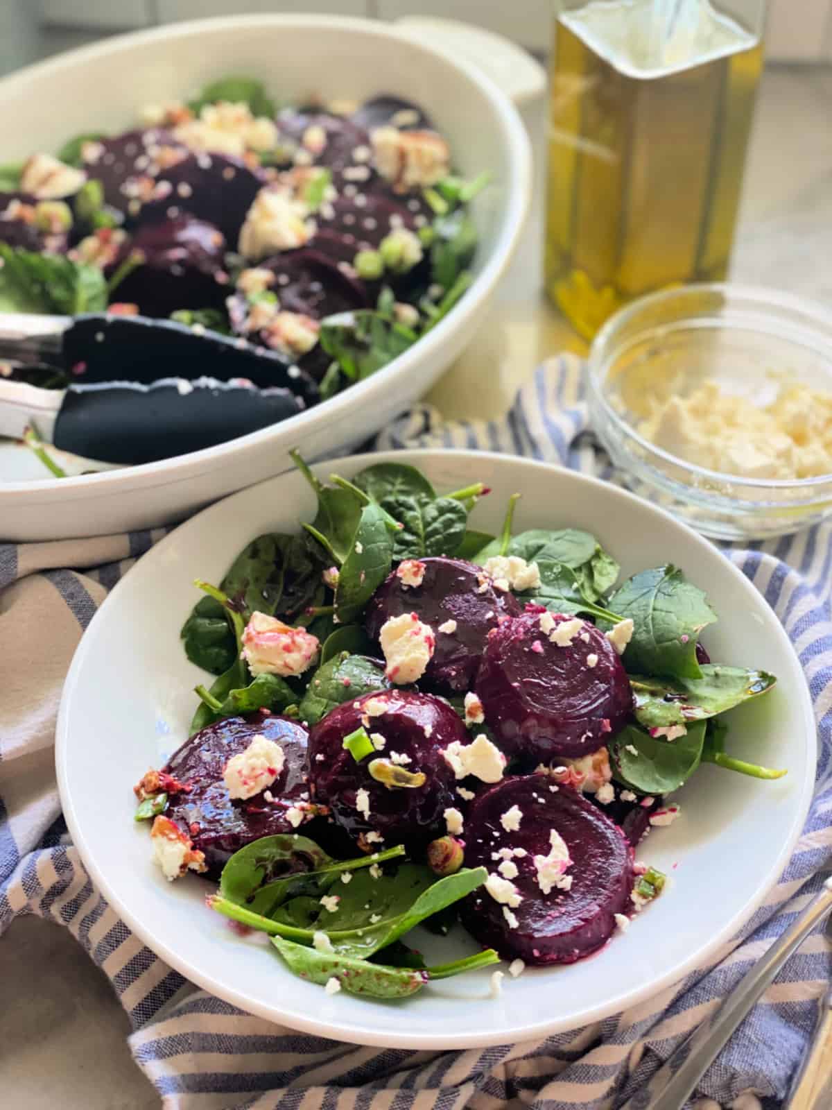 White bowl filled with spinach, beets, and feta with a big oval bowl in the background.