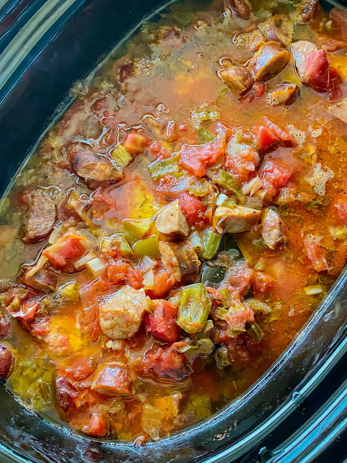 Black oval slow cooker with sausage and vegetables.