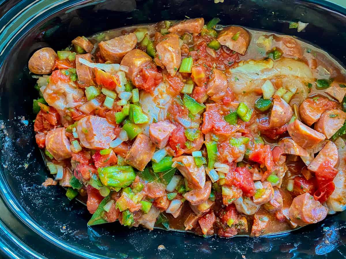Black oval slow cooker with sausage, onions, peppers, and tomatoes.