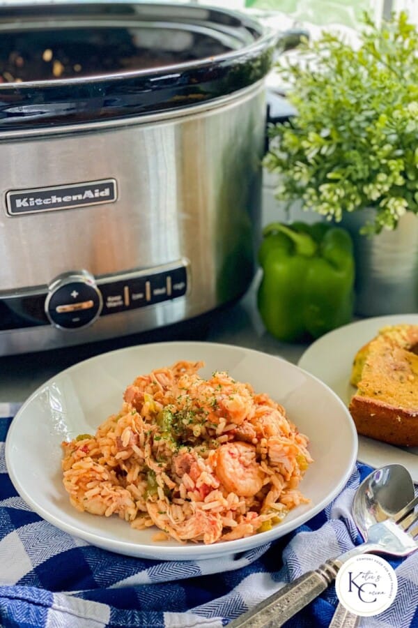 White bowl filled with rice and shrimp with ssilver slow cooker in the background.