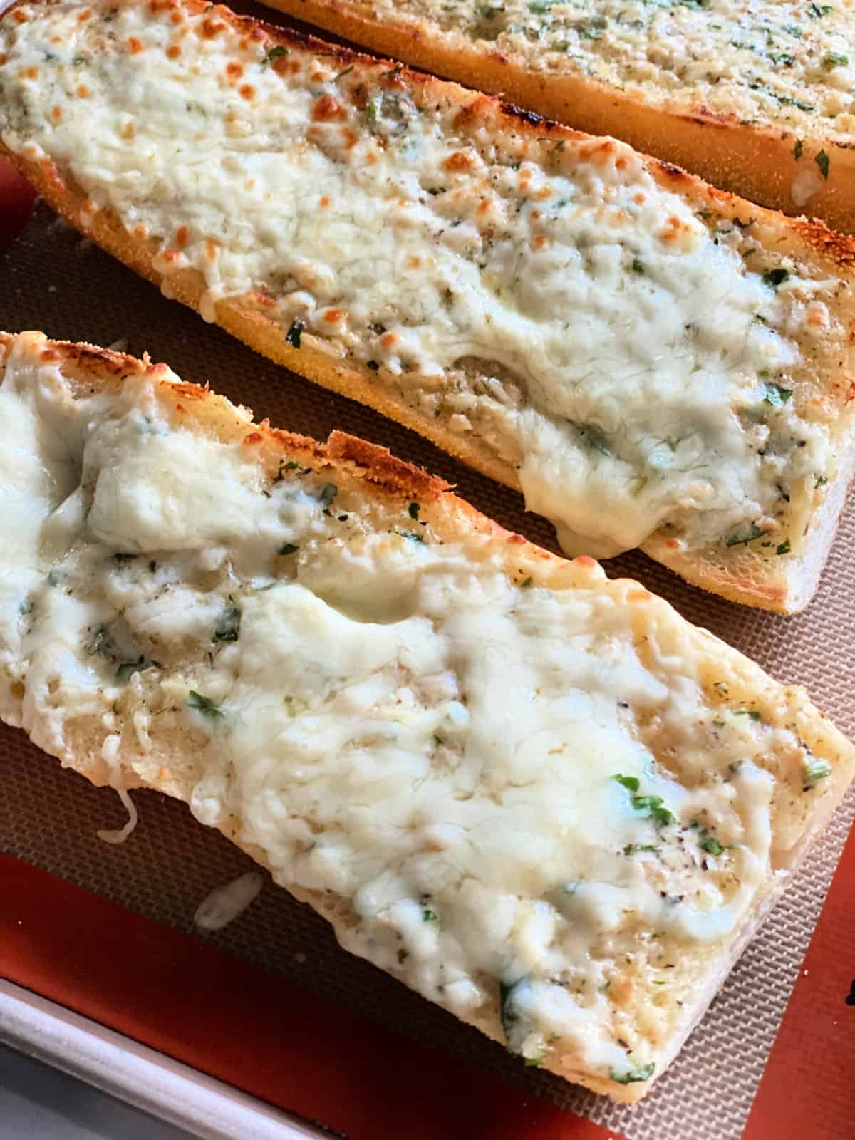 Three loaves of bread toasted with cheese on them sitting on a baking sheet.