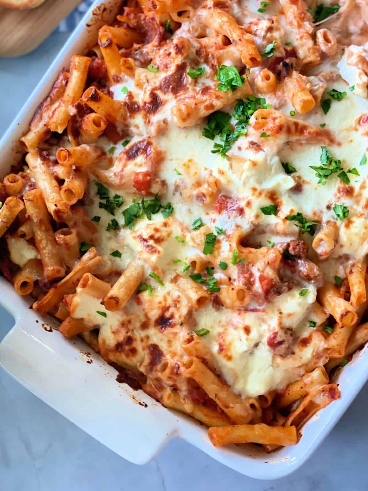 White baking dish with baked ziti noodles and cheese.