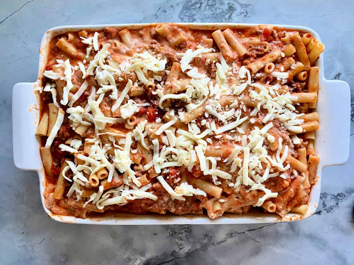 White casserole dish filled with baked ziti with shredded cheese on top.