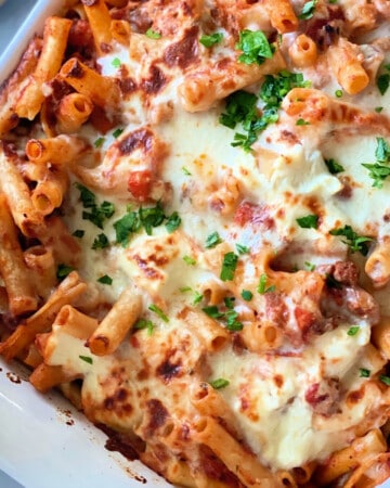 White pan filled with baked ziti, cheese, and parsley.