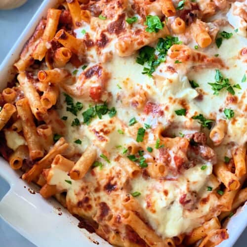 White pan filled with baked ziti, cheese, and parsley.