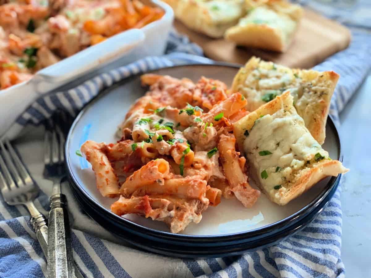 White plate filled with baked ziti and garlic cheese bread.