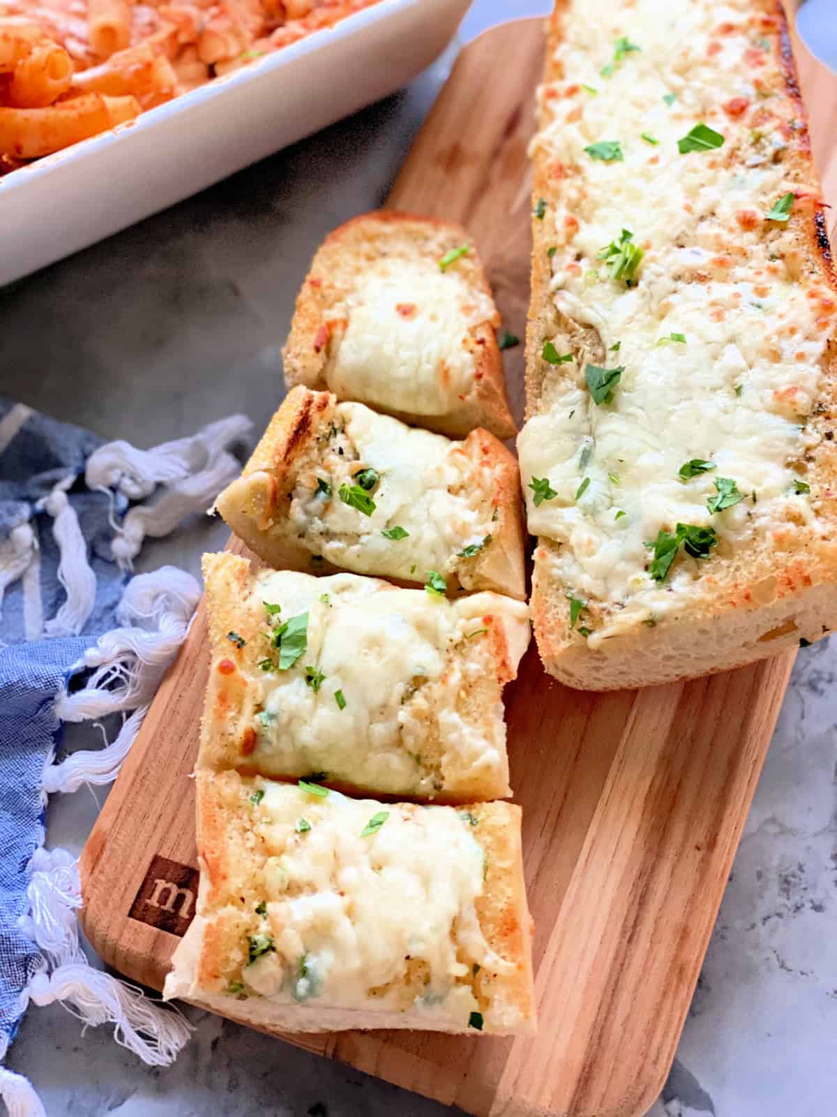 Two loaves of baked cheese bread on a wood cutting board. One loaf cut in four pieces.