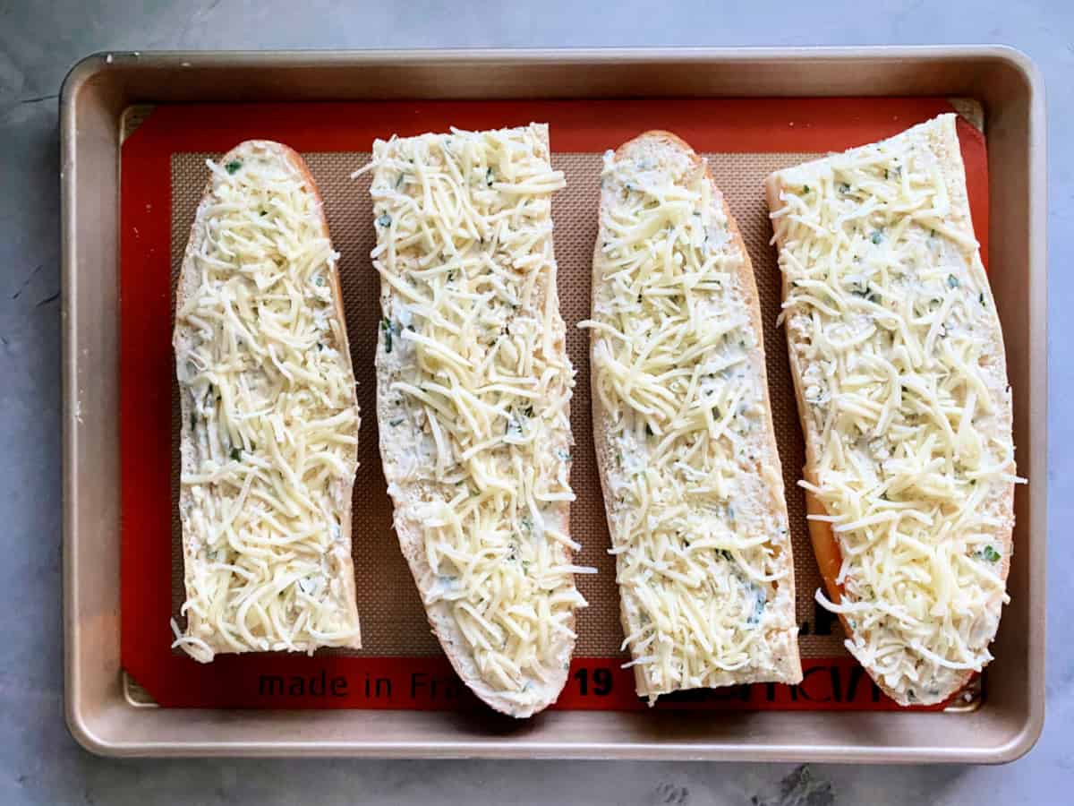 Four loaves of bread with butter and cheese resting on a bking sheet.