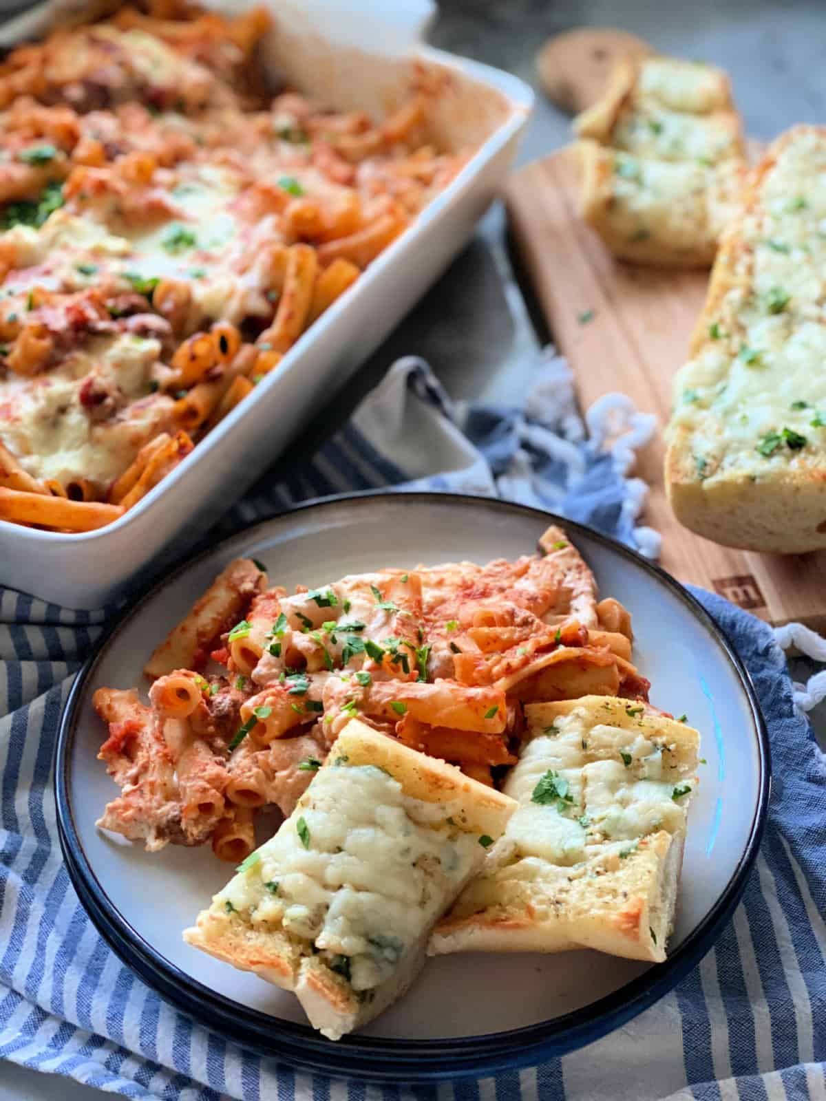 White and blue plate filled with baked ziti and two slices of garlic bread.