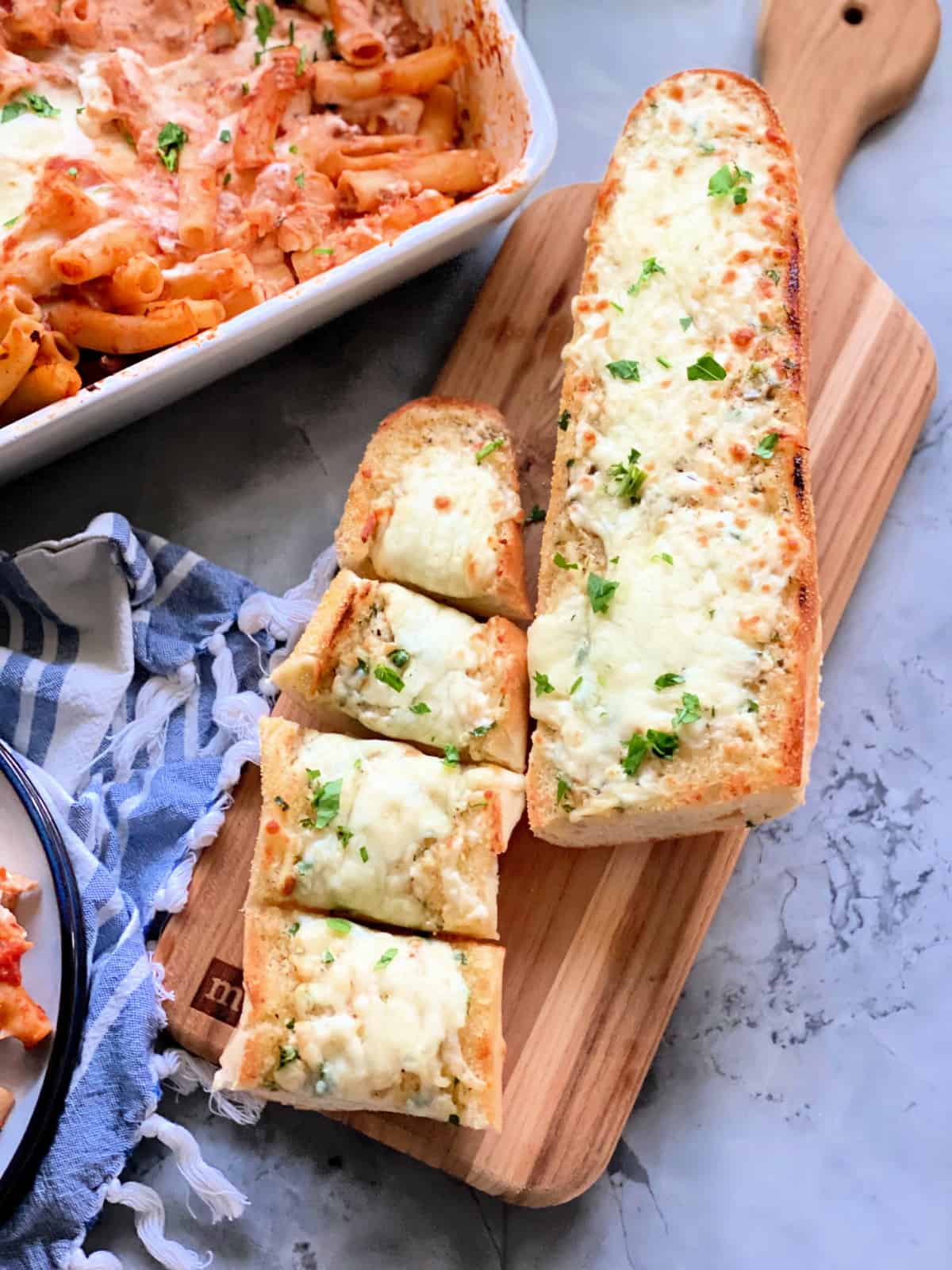 Overhead photo of two slices of cheese bread on a wood cutting board sitting on a marble countertop.