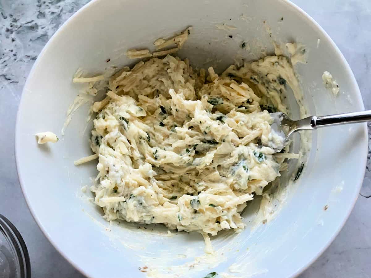 White bowl filled with cheese, butter, and herbs mixed together.