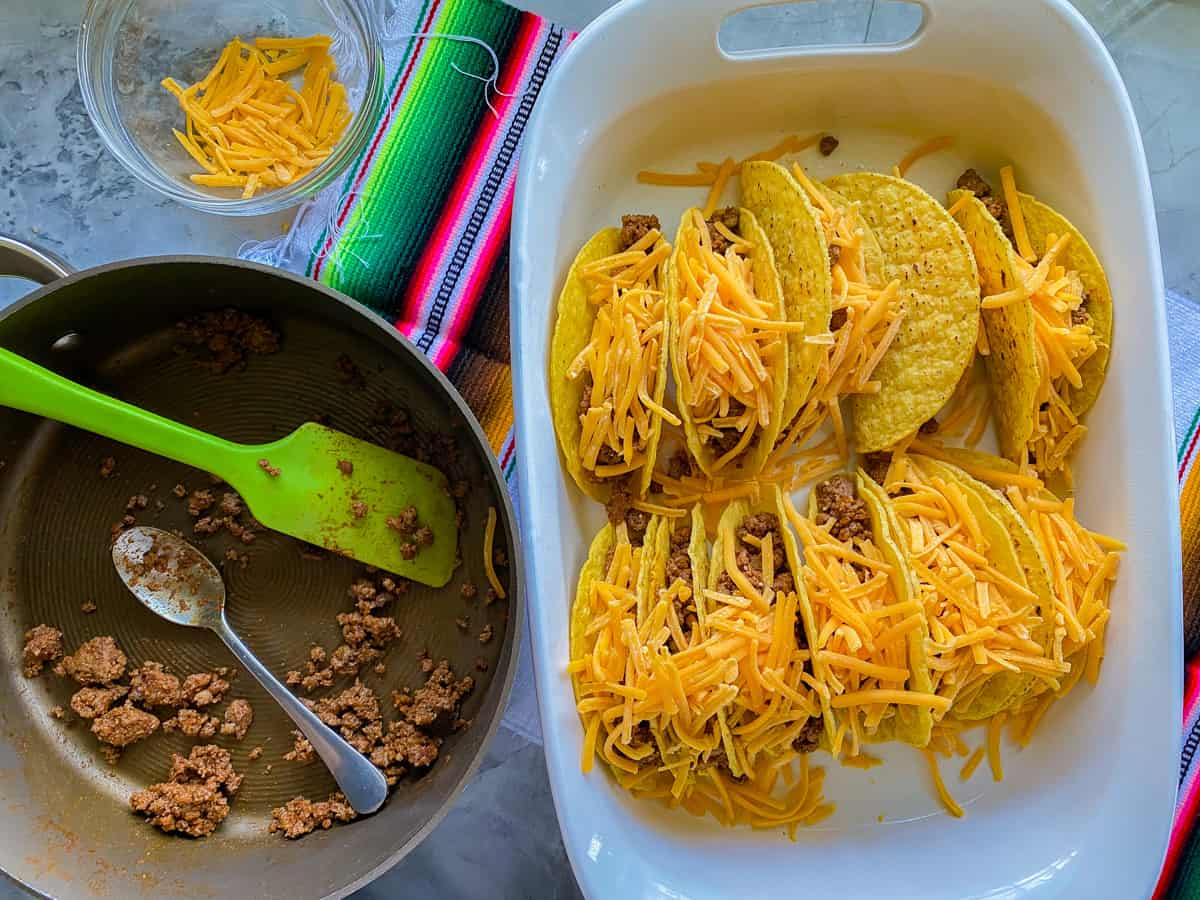 Beef Tacos resting in a white baking dish next to a pot of ground beef.