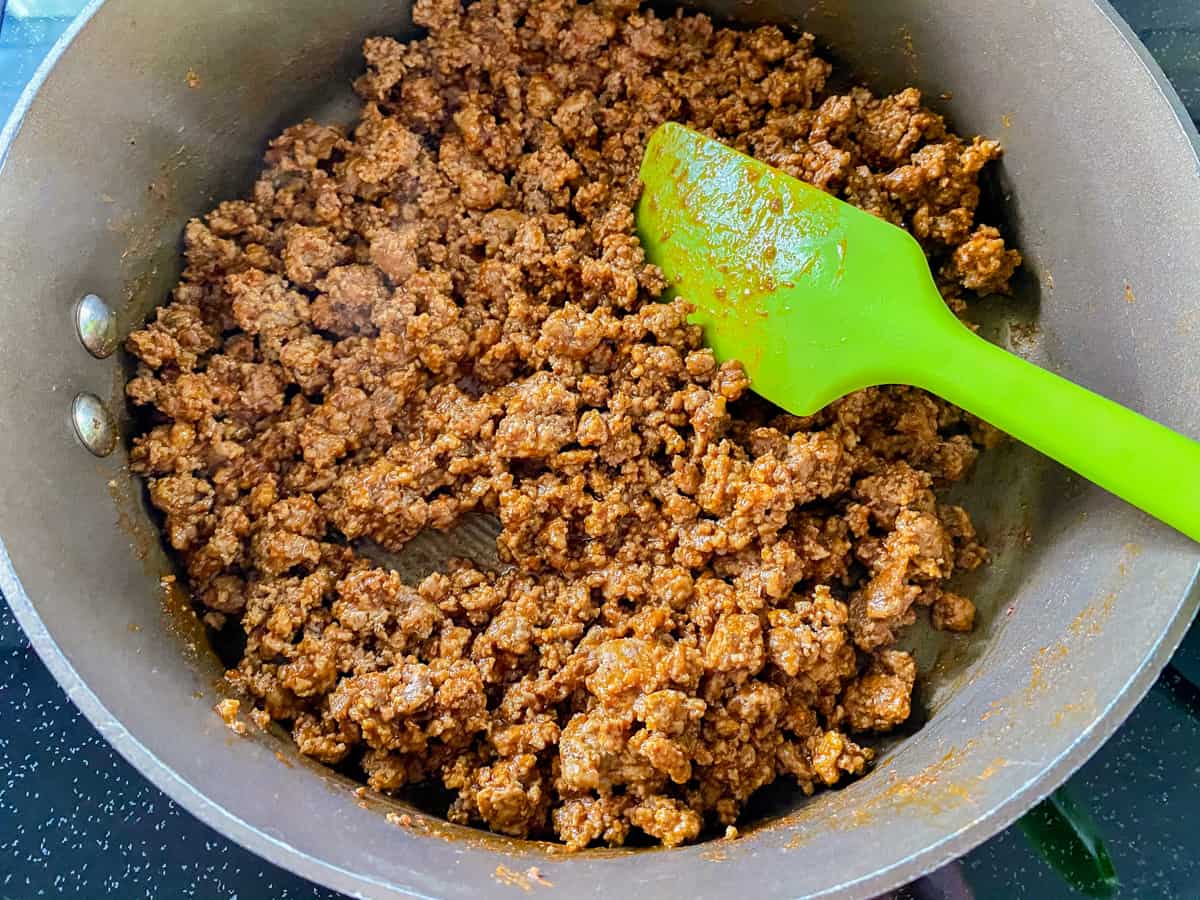 Close up shot of ground beef in a pot being stirred by a green spatula.