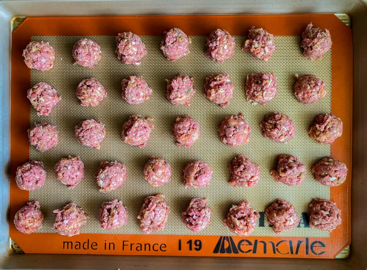 Raw mini meatballs on a silicone lined baking sheet.