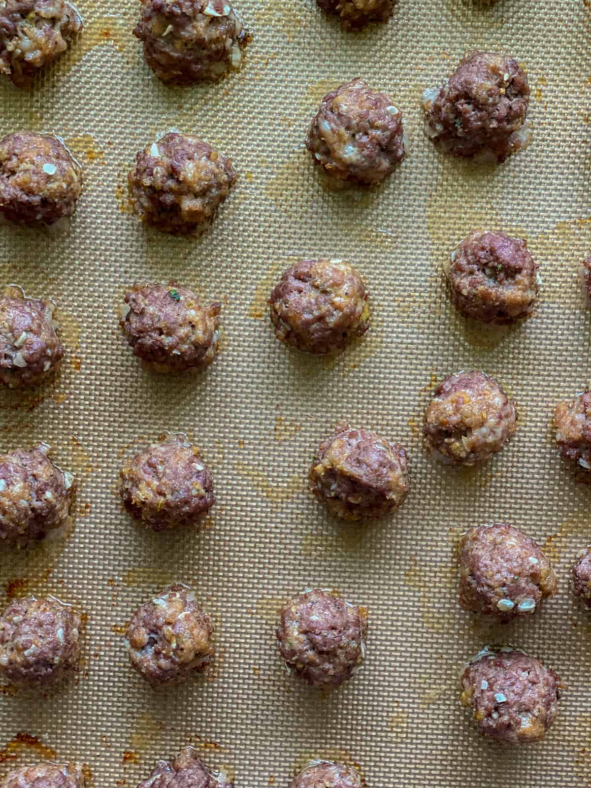 Cooked meatballs on a silicone lined baking sheet.