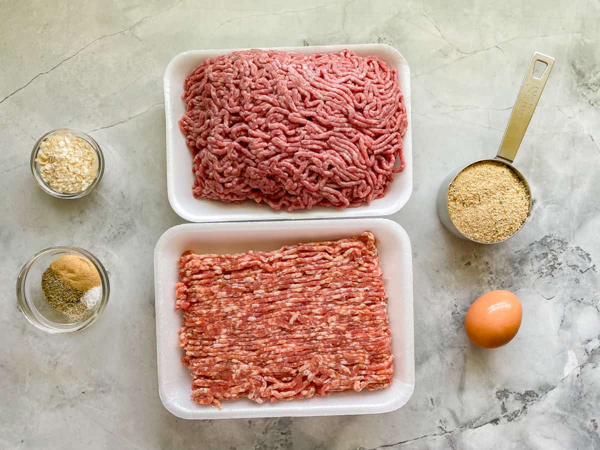Ingredients on counter: ground beef, ground pork, breadcrumbs, seasonings, onions, and egg.