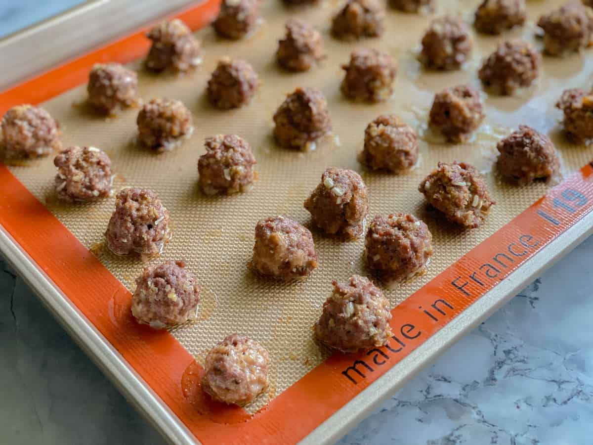 Gold baking sheet with silicone liner and cooked meatballs on top.