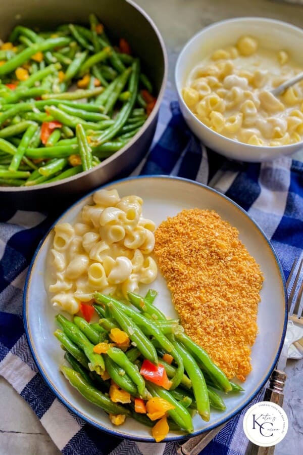 Cooked green beans served on a plate with pasta and chicken., with more green beans and pasta in the background.