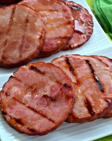 6 slices of ham steaks on a white platter with grill marks.