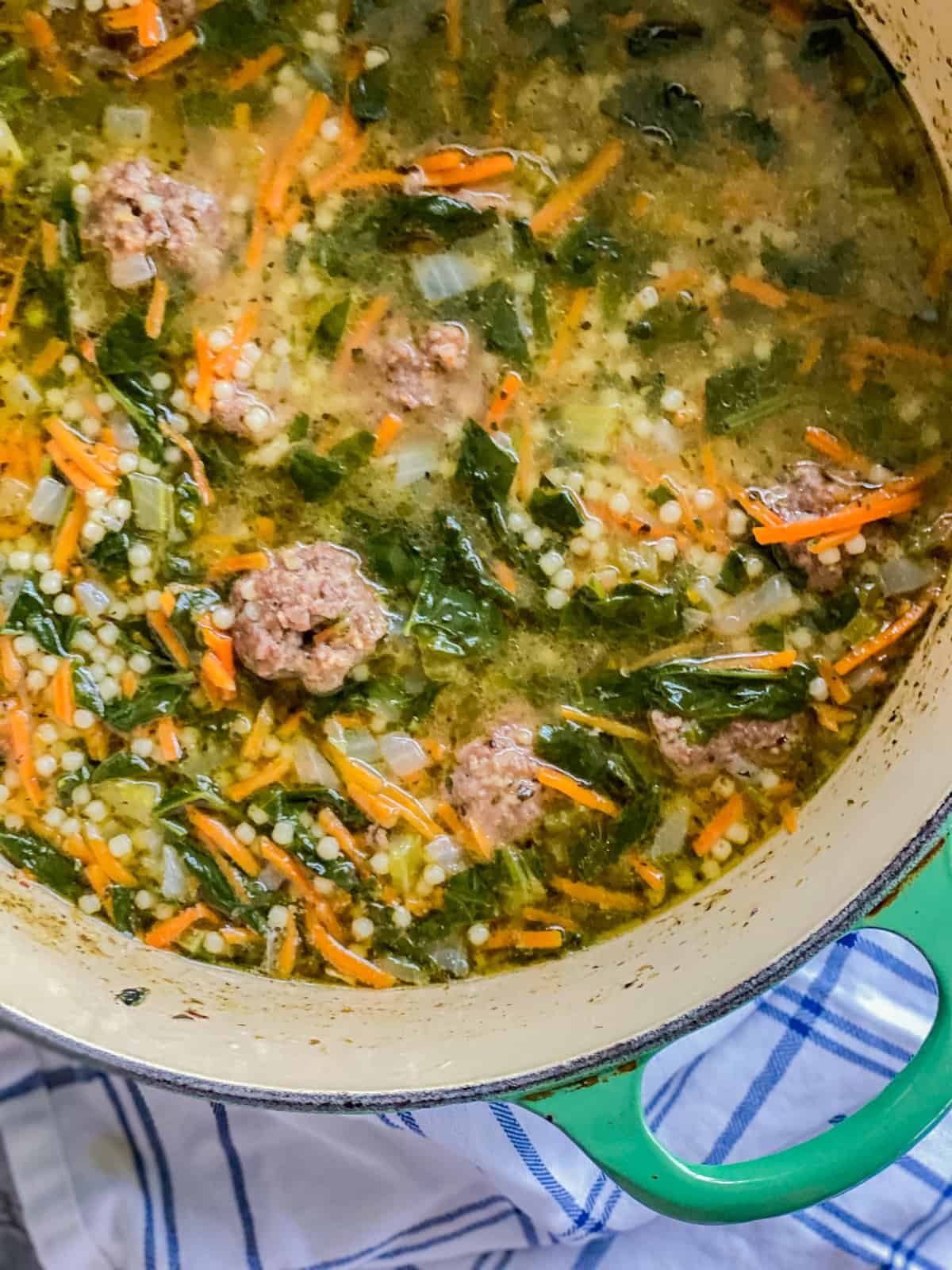 Pot of soup filled with shredded carrots, spinach, meatballs.