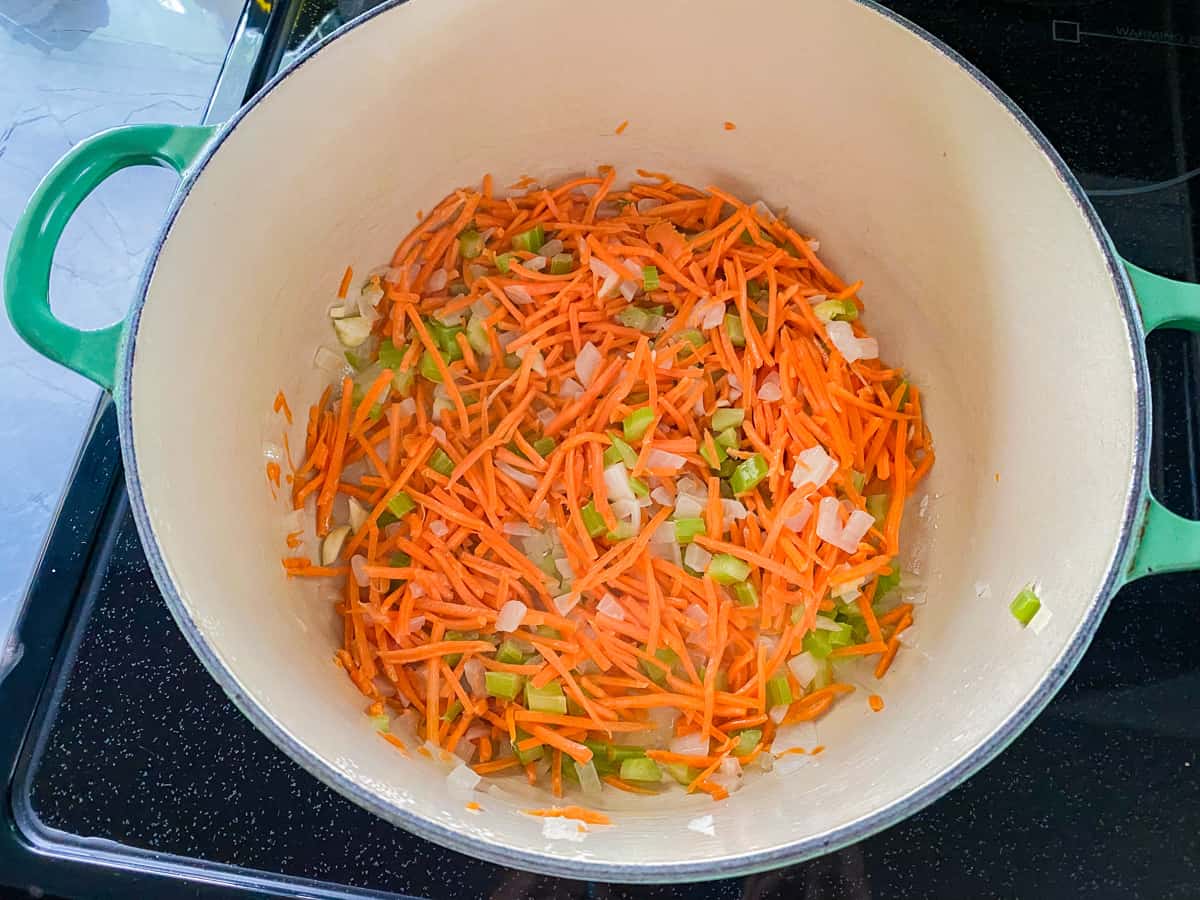 Green pot filled with shredded carrots, diced celery, and diced onions on a black stove top.