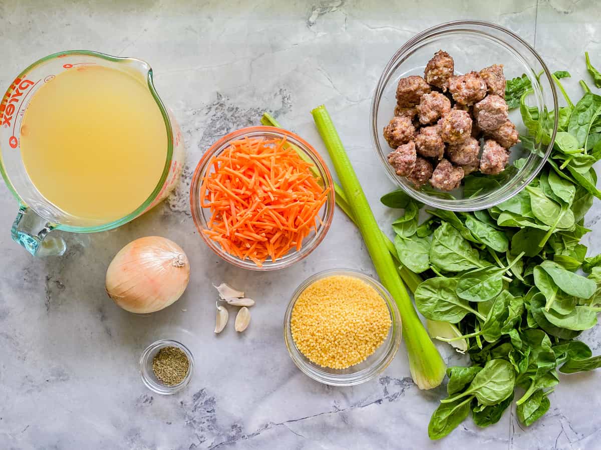 Ingredients on counter: broth, onion, carrots, pastina, garlic, spices, celery, meatballs, and spinach.