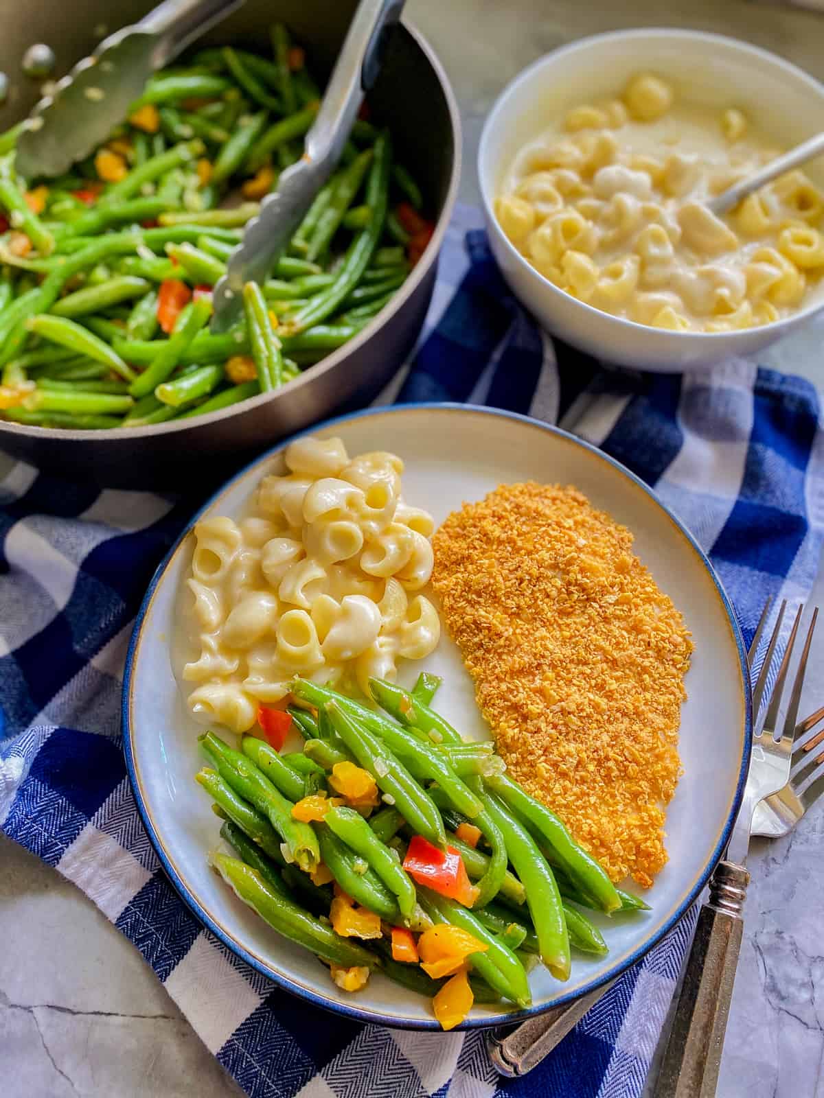 Cooked green beans served on a plate with pasta and chicken., with more green beans and pasta in the background.
