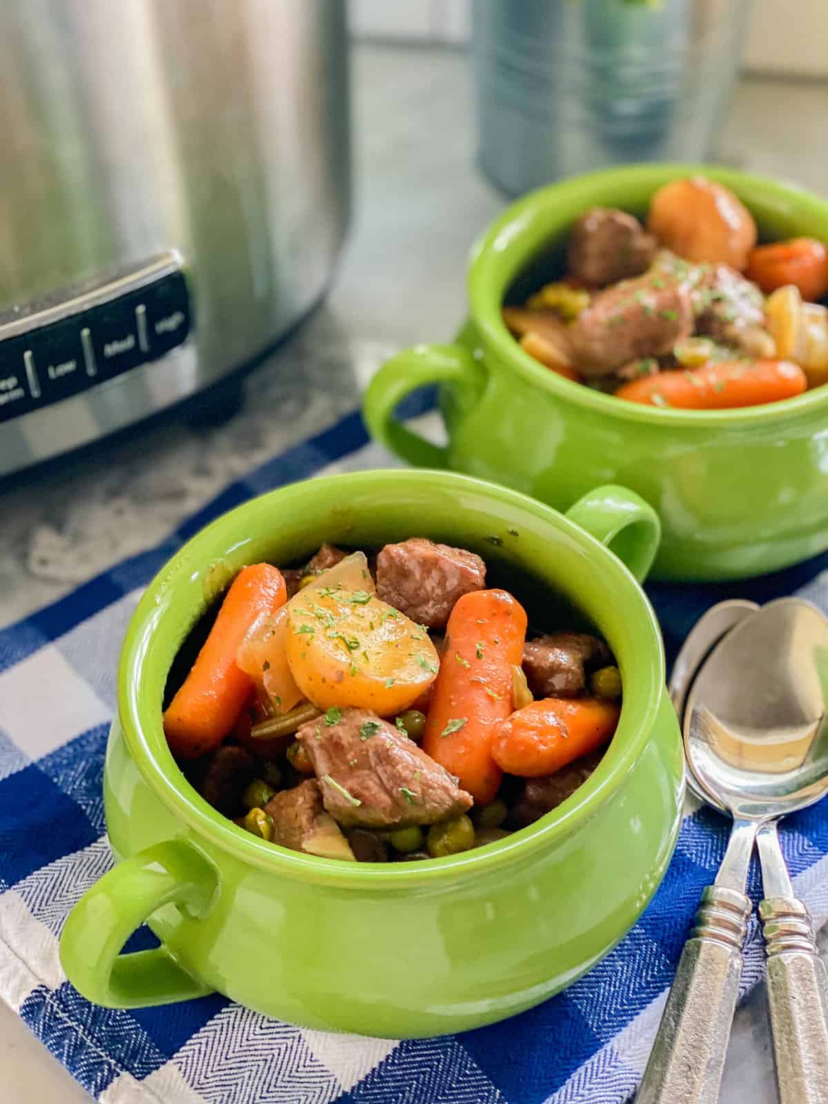 Close up photo of the slow cooked beef stew served in two mini green pots.