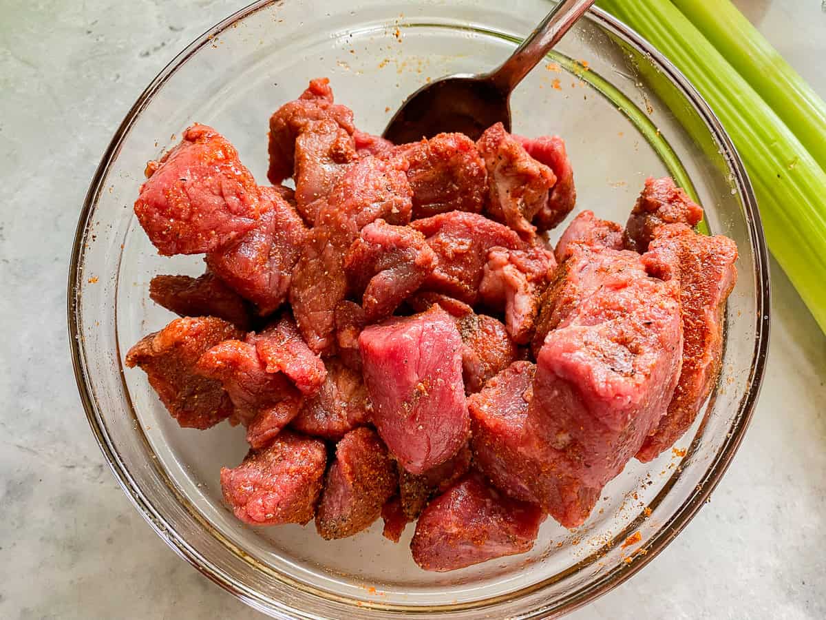 Beef stew being seasoned in a mixing bowl.