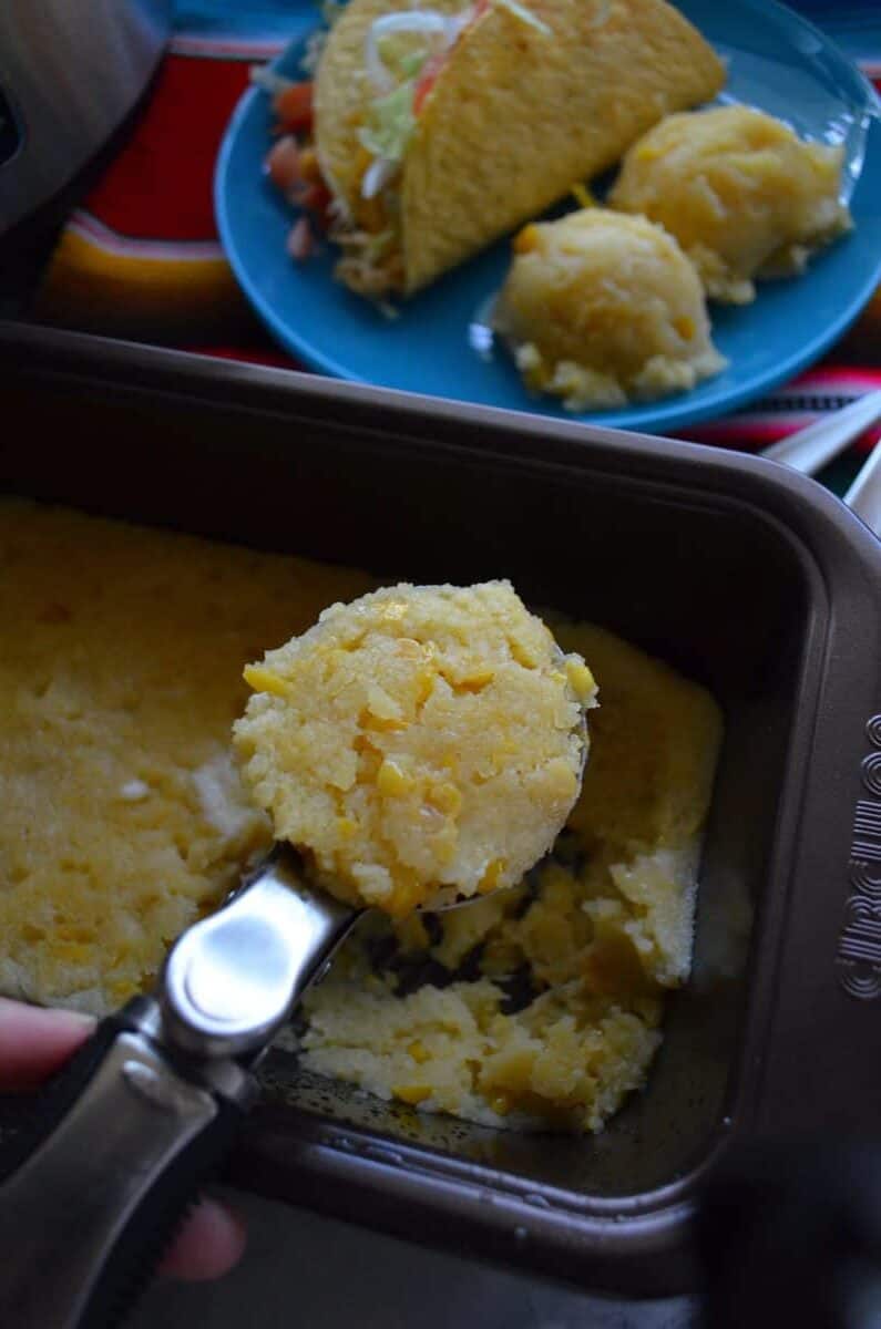 Hand holding an ice cream scoop with corn batter in scoop.