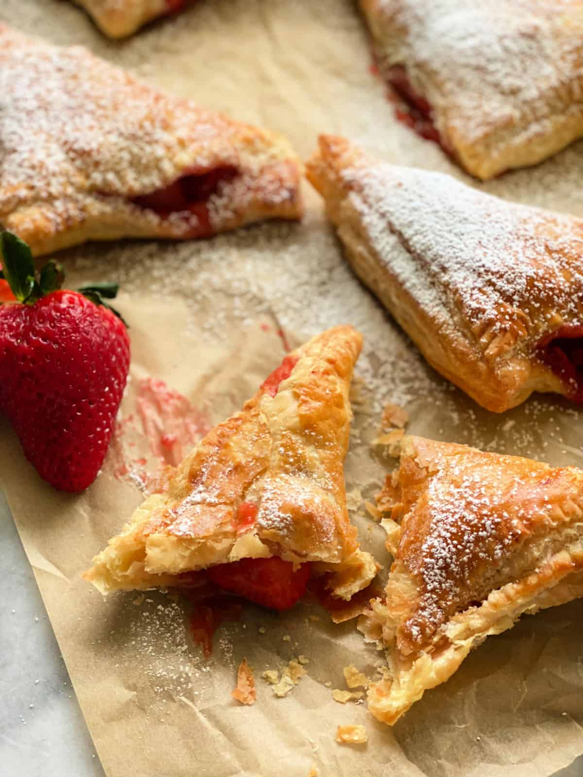 Strawberry turnover cut in half on brown parchment paper.