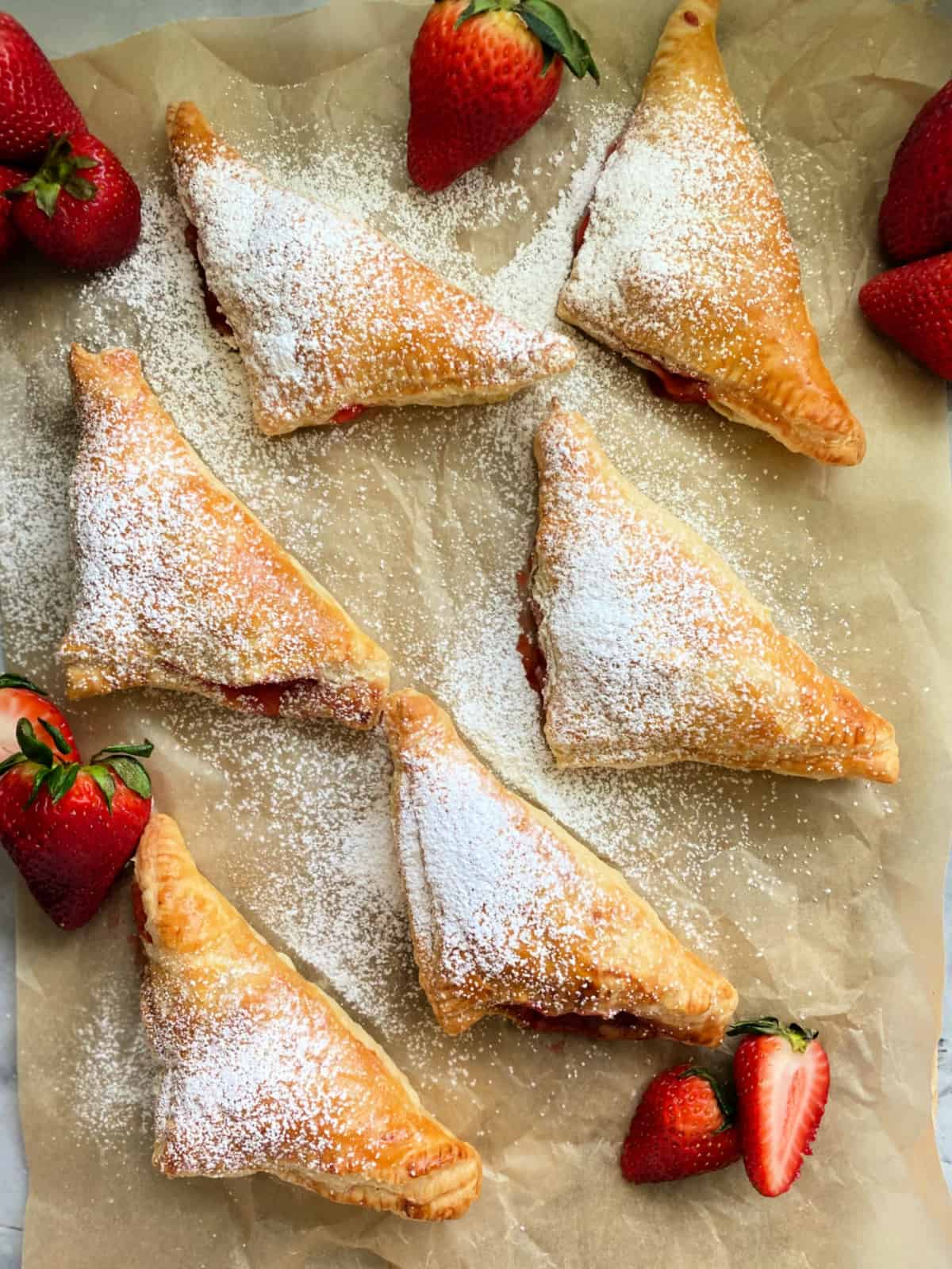 6 puff pastry turnovers on a brown parchment paper sprinkled with powdered sugar.